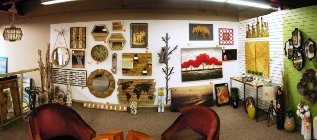 A white wall inside a store with paintings and other decorative wooden items for sale